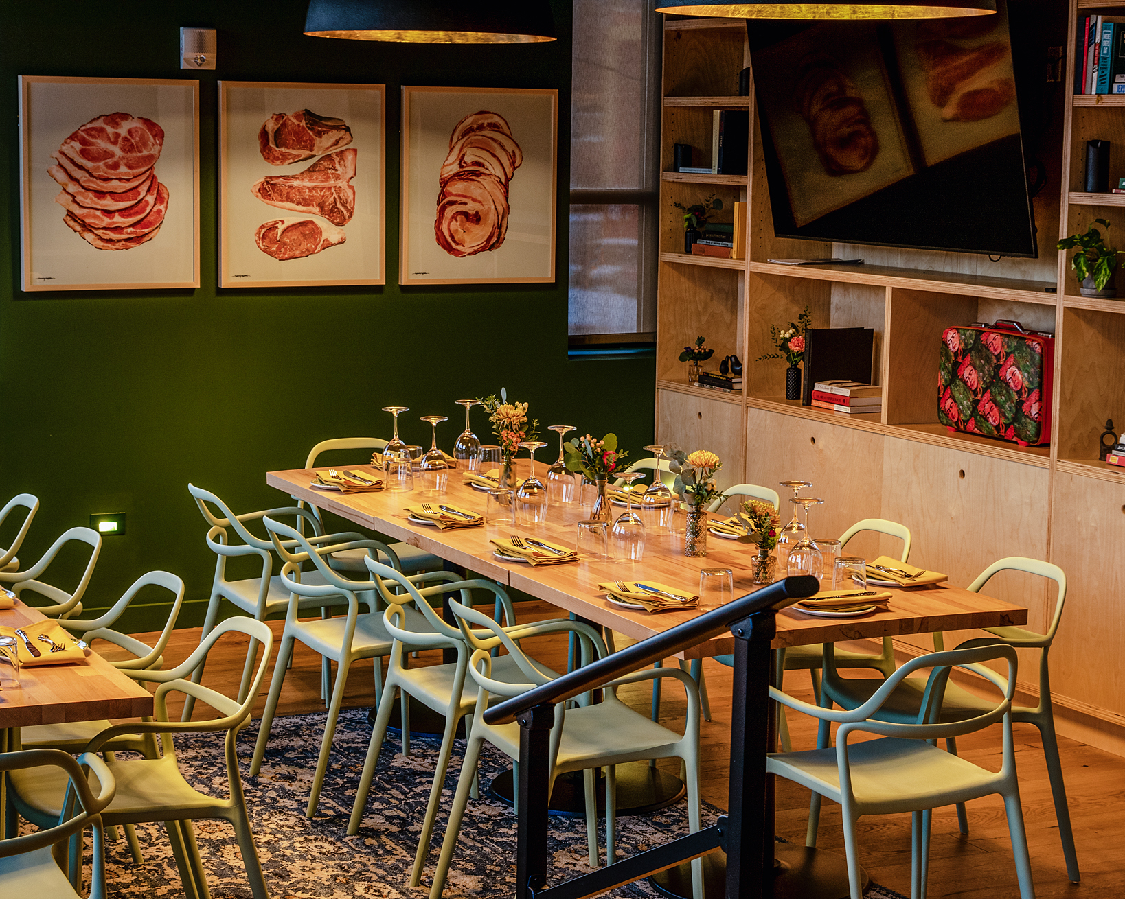 The Green Room — deep green walls, gold-lined pendants, and a communal table set with butcher-print art